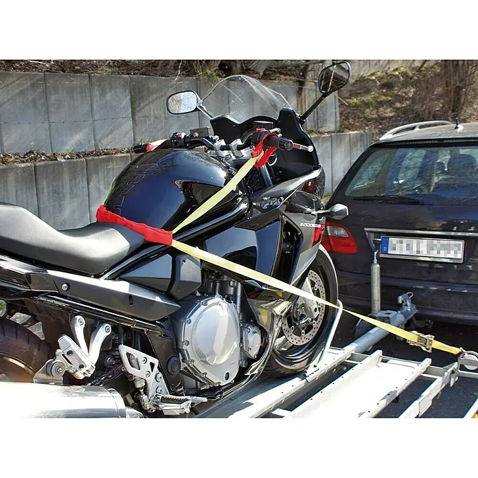LAS Spanngurtsystem - Geeignet für: Motorräder, 6 -tlg. - Das Bild zeigt ein Motorrad, das mit gelben Spanngurten und einem roten Schutz auf einem Anhänger befestigt ist, um einen sicheren Transport zu gewährleisten.