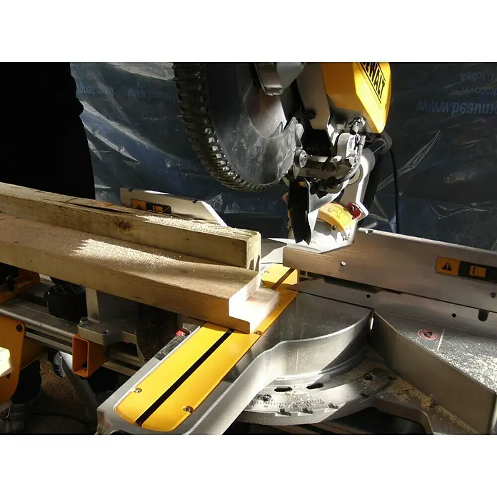 DeWalt Paneelsägen-Set DWS780KIT - 1.675 W, 0 U/min - 3.800 U/min, Durchmesser Sägeblatt: 305 mm - Nahaufnahme einer gelben DEWALT-Kappsäge, die ein Holzbrett durchschneidet. Späne fliegen, während die Säge präzise arbeitet.