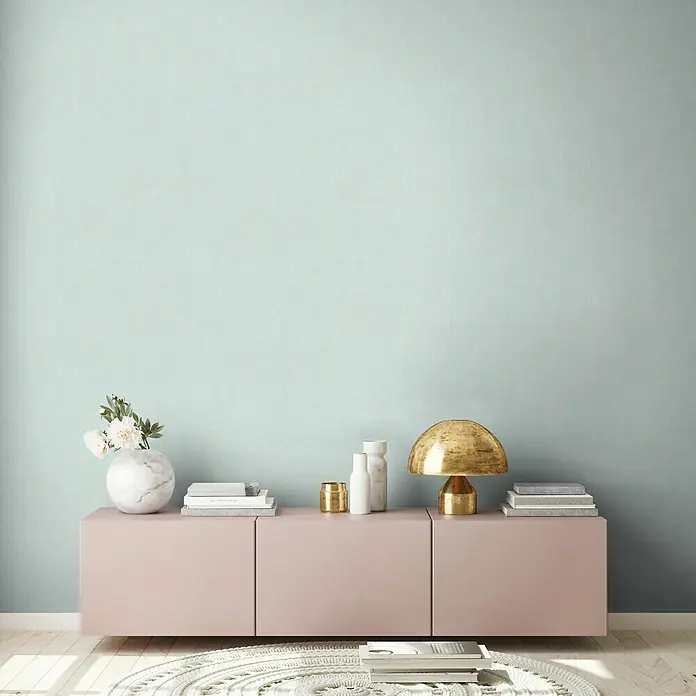 A.S. Création New Walls Vliestapete Textil - Türkis, Uni, 10,05 x 0,53 m - Nahaufnahme eines modernen Wohnzimmers mit einer eleganten rosa Kommode, die mit stilvollen Dekorationsgegenständen geschmückt ist.