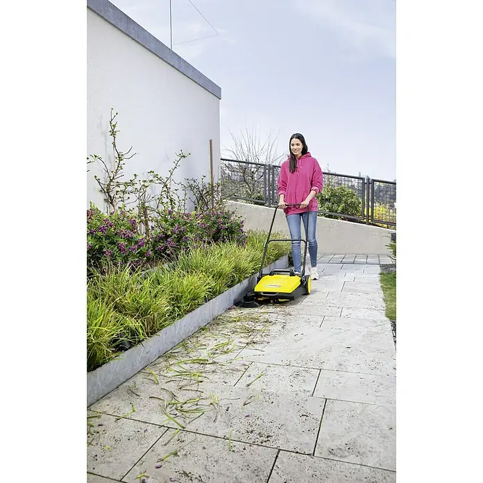 Kärcher Handkehrmaschine S 4 - Flächenleistung: 1.800 m²/h, 20 l - Frau reinigt eine Auffahrt mit der gelben Kärcher S 650 2-in-1 Kehrmaschine, die Schmutz effizient aufnimmt.