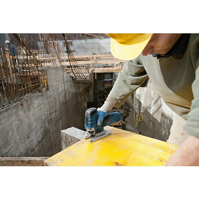 Bosch Professional Elektro-Pendelhubstichsäge GST 150 CE - 780 W, 500 /min - 3.100 /min, Anzahl Pendelhubstufen: 4 Stk. - Ein Bauarbeiter mit Schutzhelm benutzt eine blaue Bosch Stichsäge, um Holz auf einer Baustelle zuzuschneiden.