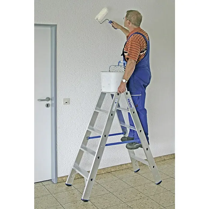 Krause Stabilo Doppelleiter - Anzahl Tritte: 10 Stk., Arbeitshöhe: 2,7 m, Aluminium - Mann auf einer Krause Leiter, der eine Wand streicht, mit Farbeimer und Farbroller, ideal für Renovierungsarbeiten.