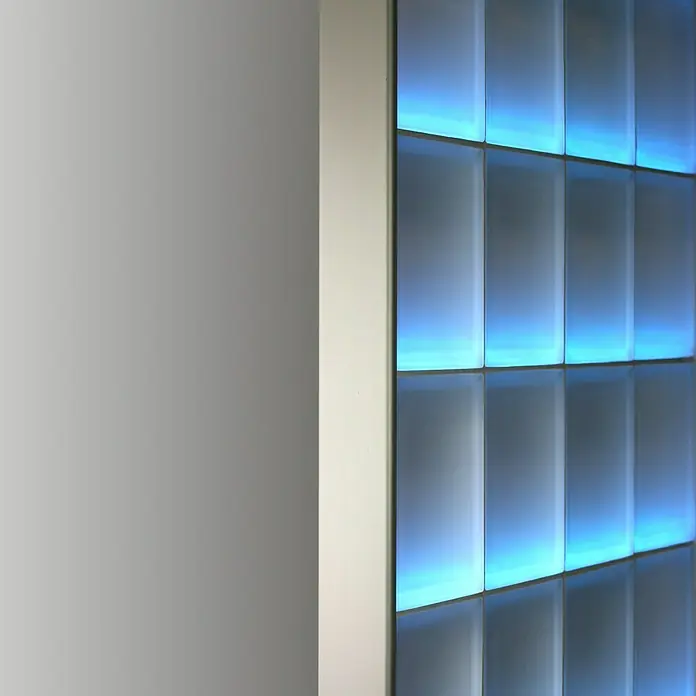 Fuchs Design Glasbausteinprofil - Aluminium, Satiniert, 125 x 8,5 cm - Nahaufnahme einer Wand mit quadratischen blauen Lichtelementen, die ein modernes und stilvolles Design ausstrahlen.