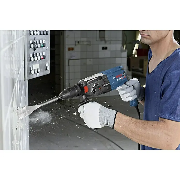 Bosch Professional Kombihammer GBH 2-28 F - 880 W, 3,2 J, SDS-Plus-Aufnahme, Inkl. 3 x Bohrer & Meißel - Ein Mann benutzt einen Boschhammer, um Fliesen abzuschlagen. Die Bohrmaschine ist blau und schwarz und wird mit Handschuhen bedient.