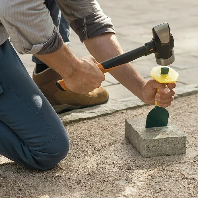 Fiskars Fäustel L - Gewicht Kopf: 1.800 g, Material Stiel: Glasfaserverstärkter Kunststoff (GfK) - Ein Mann benutzt einen Hammer und einen Meißel, um einen Stein zu bearbeiten. Werkzeuge für die Bearbeitung von Steinen im Einsatz.