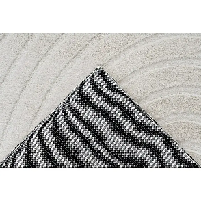Fellteppich Zen - Ivory, 150 x 80 cm, 100 % Polyester - Nahaufnahme eines flauschigen, hellgrauen Teppichs mit gewelltem Muster und einer dunklen, strukturierten Rückseite, der aufgerollt ist.