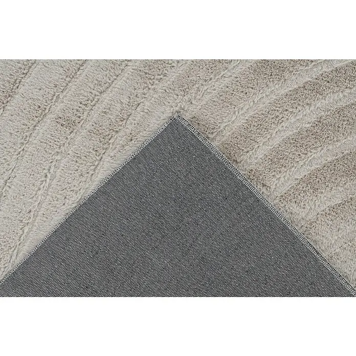 Fellteppich Zen - Light Taupe, 170 x 120 cm, 100 % Polyester - Detailaufnahme eines hellgrauen Teppichs mit gewellter Textur und einer grauen, texturierten Rückseite, die einen Einblick in die Verarbeitung bietet.