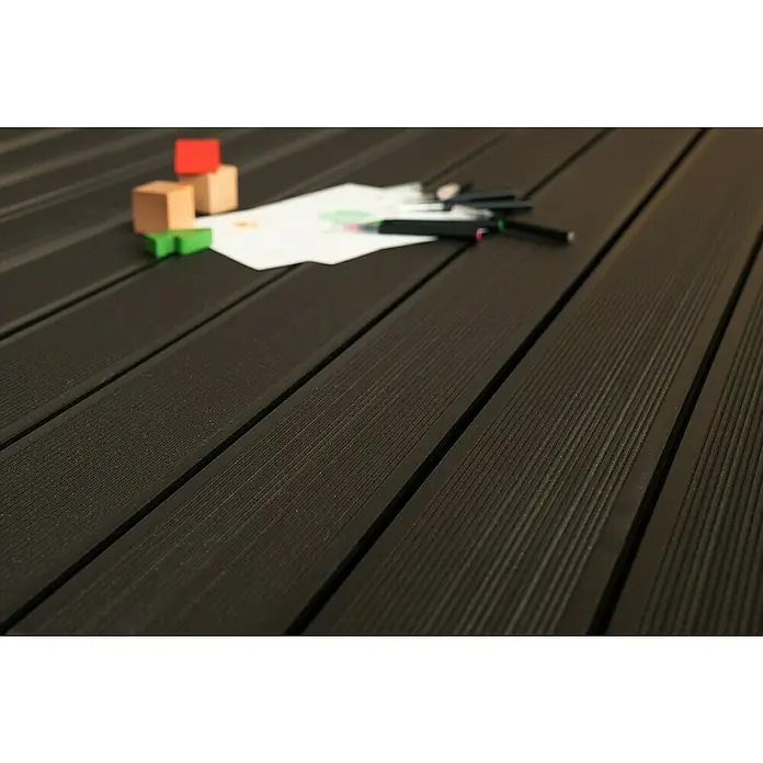 WPC-Terrassendiele Artwood - 300 x 12 x 2,8 cm, Grau - Nahaufnahme einer dunklen Terrassendiele mit Spielzeug und Stiften. Die Holzstruktur ist gut sichtbar, wodurch ein rustikaler Look entsteht.