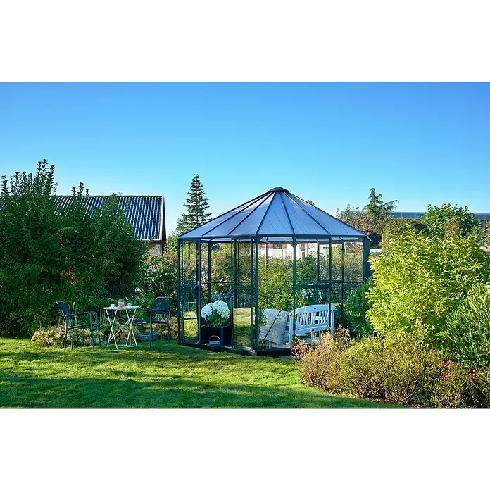 Halls Gewächshaus Atrium - Außenmaß inkl. Dachüberstand (B x T): 380 x 380 cm, Material Seitenwand: Glas, 3 mm, Grün - Das Bild zeigt ein Gewächshaus im Garten, das mit Pflanzen gefüllt ist. Daneben stehen Tisch und Stühle.