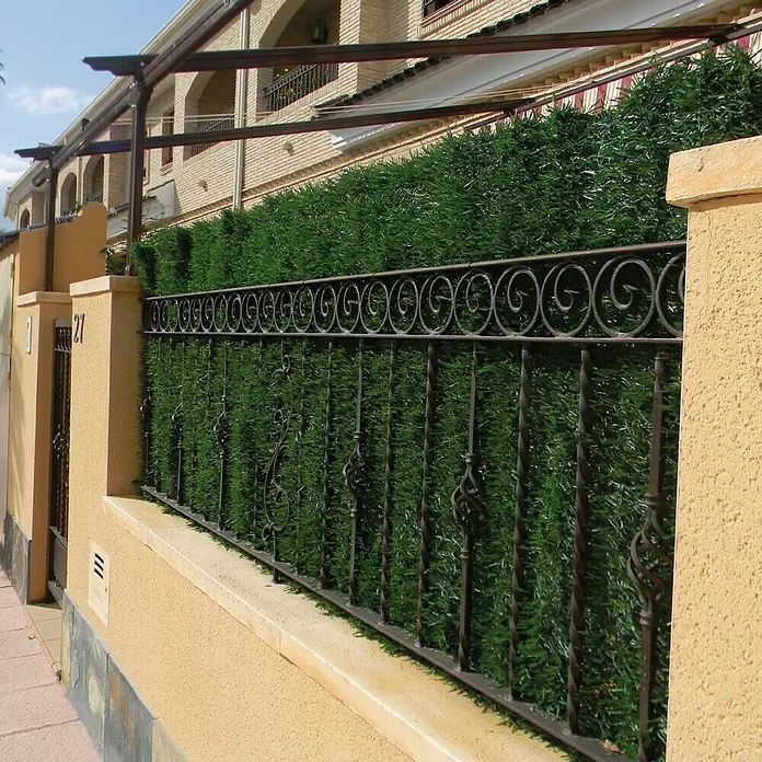 Faura Malla de ocultación seto artificial Hoja Ancha - 3 x 2 m, Verde - Primer plano de una valla de jardín con vegetación artificial exuberante, que ofrece privacidad y un toque decorativo.
