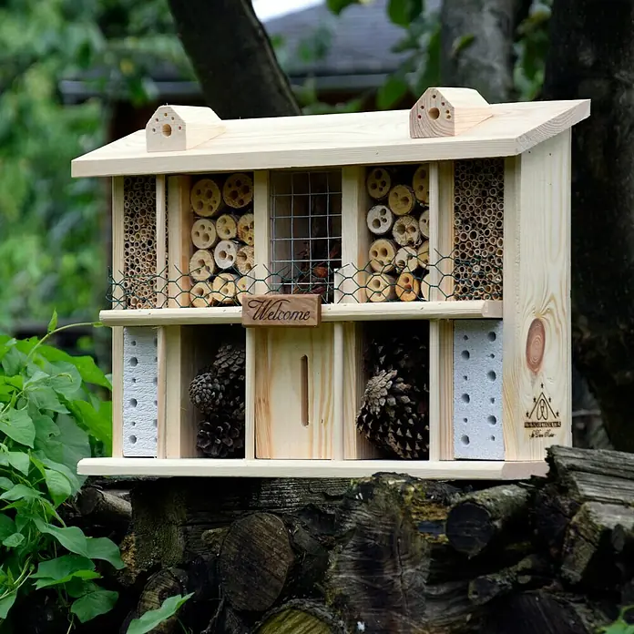 Dobar Insektenhotel Landsitz SuperiorBastelset, 47 x 12,5 x 34 cm, Kiefer - Ein detailreiches Insektenhotel aus Holz mit verschiedenen Füllmaterialien, das auf einem Holzstapel im Garten steht.