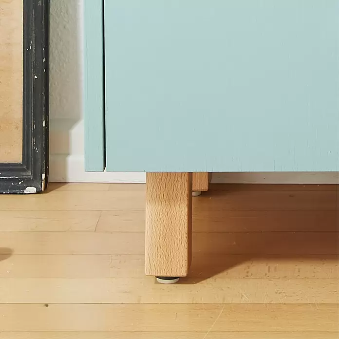 Wagner System Möbelfuß Classic ST 7810 - L x B x H: 60 x 60 x 110 mm, Holz - Unterer Teil eines hellblauen Schranks mit Beinen aus Naturholz auf Holzboden.