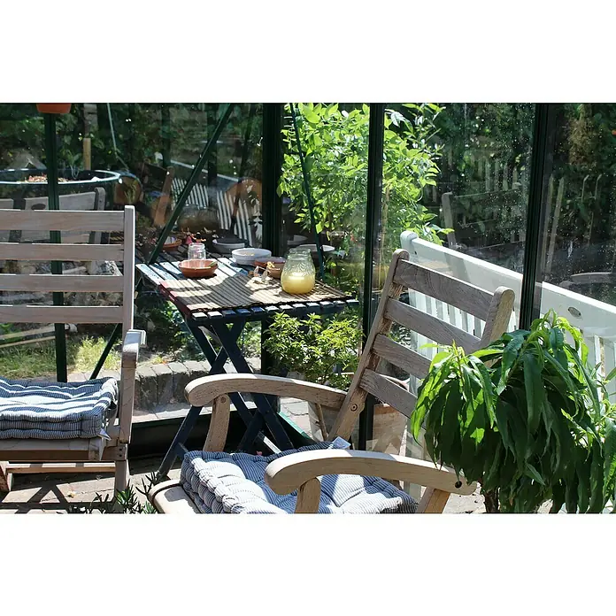 Juliana Gewächshaus Compact - Außenmaß inkl. Dachüberstand (B x T): 224 x 296 cm, Material Seitenwand: Glas, 3 mm, Schwarz - Einladende Gartenszene mit zwei Stühlen und einem Tisch in einem Gewächshaus, ideal für entspannte Stunden im Grünen.