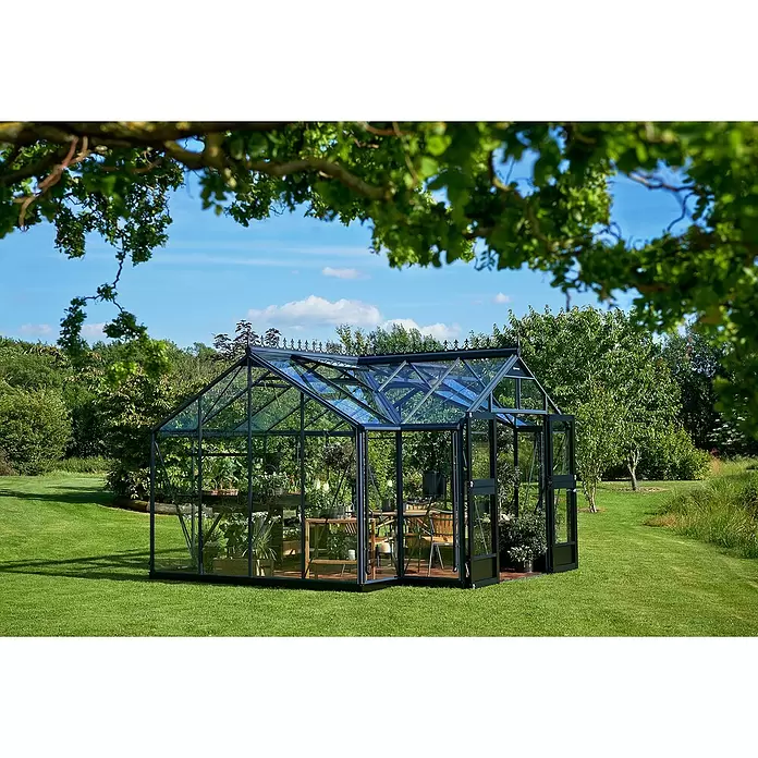 Juliana Gewächshaus Orangerie - Außenmaß inkl. Dachüberstand (B x T): 439 x 296 cm, Material Seitenwand: Glas, 3 mm, Anthrazit - Dunkel gerahmtes Glasgewächshaus im Garten, gefüllt mit Pflanzen und Gartenmöbeln.