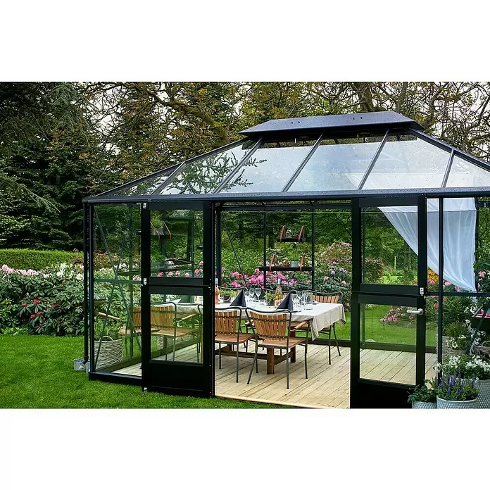 Juliana Gewächshaus Grand Oase - Außenmaß inkl. Dachüberstand (B x T): 439 x 296 cm - Ein schwarz gerahmtes Glashaus mit Holzboden, als Essbereich im Garten genutzt.