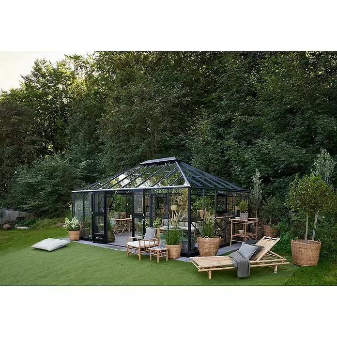 Juliana Gewächshaus Grand Oase - Material Seitenwand: Glas, 3 mm, Anthrazit - Modernes Gewächshaus mit schwarzem Rahmen und Glaspaneelen im Garten, möbliert mit Bambussitzgelegenheiten.