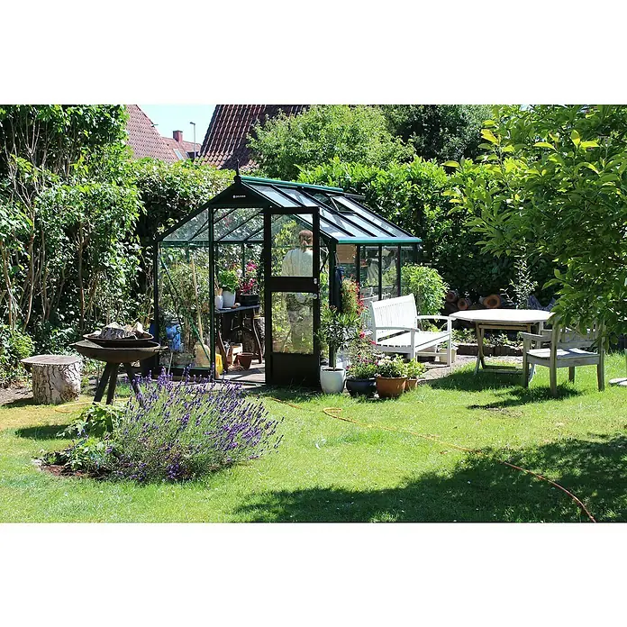 Juliana Gewächshaus Compact - Außenmaß inkl. Dachüberstand (B x T): 224 x 368 cm, Material Seitenwand: Glas, 3 mm, Schwarz - Ein Juliana Gewächshaus im Garten, umgeben von üppigem Grün, mit einem offenen Eingang und Gartenmöbeln im Hintergrund.