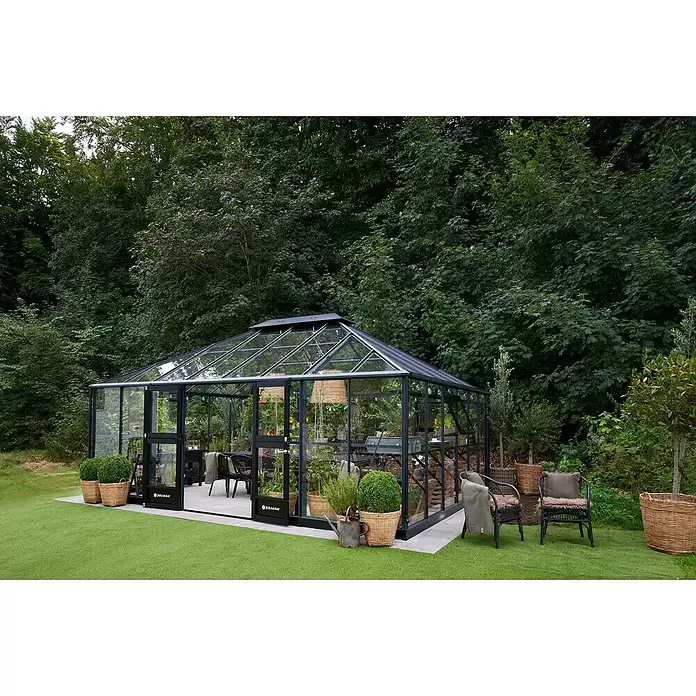 Juliana Gewächshaus Grand Oase - Material Seitenwand: Glas, 3 mm, Anthrazit - Großes schwarzes Gewächshaus mit Glaswänden, innen möbliert, in einer grünen Gartenumgebung.