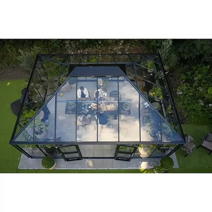 Juliana Gewächshaus Grand Oase - Material Seitenwand: Glas, 3 mm, Anthrazit - Luftaufnahme eines modernen Gewächshauses mit schwarzem Rahmen und Glas im Garten, in dem Menschen an einem Tisch speisen.