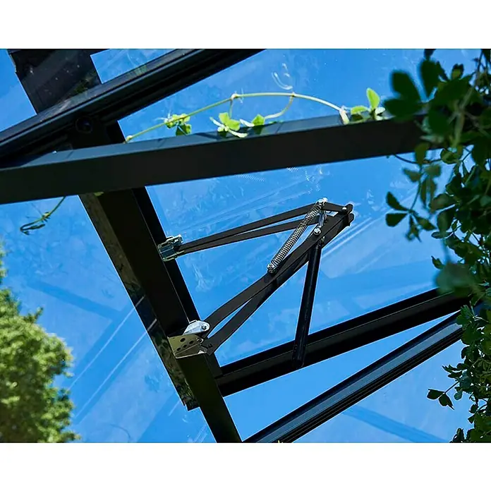 Juliana Automatischer Fensteröffner Univent - Passend für: Juliana & Halls Gewächshäuser mit Glas und Stegdoppelplatten - Detailansicht eines Gewächshausfensters mit schwarzem Rahmen und automatischem Öffnungsmechanismus, umgeben von Grünpflanzen.