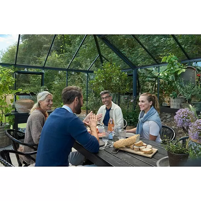 Juliana Gewächshaus Grand Oase - Material Seitenwand: Glas, 3 mm, Anthrazit - Vier Personen speisen und unterhalten sich in einem modernen Glasgewächshaus.