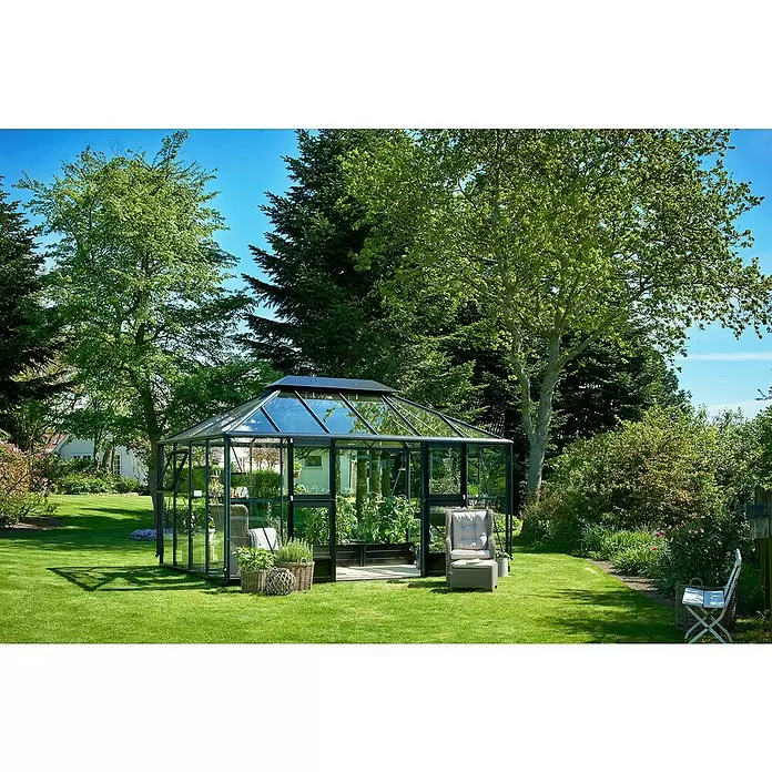 Juliana Gewächshaus Grand Oase - Außenmaß inkl. Dachüberstand (B x T): 439 x 296 cm - Dunkelgraues Gewächshaus aus Glas im sonnigen Garten, genutzt für Pflanzenanbau und als Entspannungsbereich.