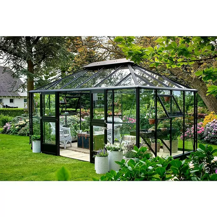 Juliana Gewächshaus Grand Oase - Außenmaß inkl. Dachüberstand (B x T): 439 x 296 cm - Großes, modernes Gewächshaus mit schwarzem Rahmen und Glas, als Gartenhaus mit Sitzgelegenheiten und Pflanzen genutzt.