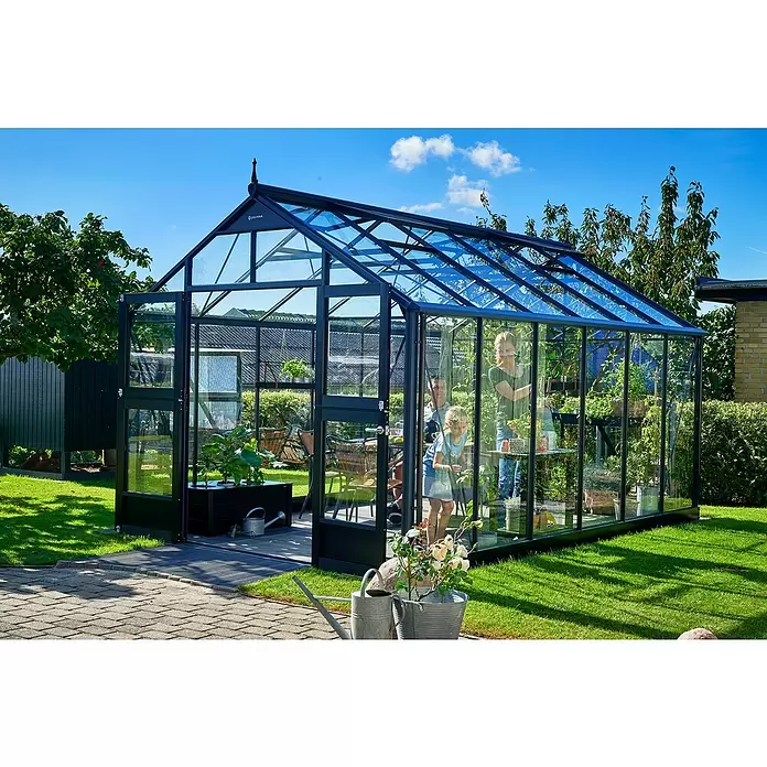 Juliana Gewächshaus Premium - Außenmaß inkl. Dachüberstand (B x T): 296 x 439 cm, 3 mm, Anthrazit, Einscheibensicherheitsglas - Großes Gewächshaus aus schwarz gerahmtem Glas in einem sonnigen Garten, eine Familie pflegt Pflanzen darin.