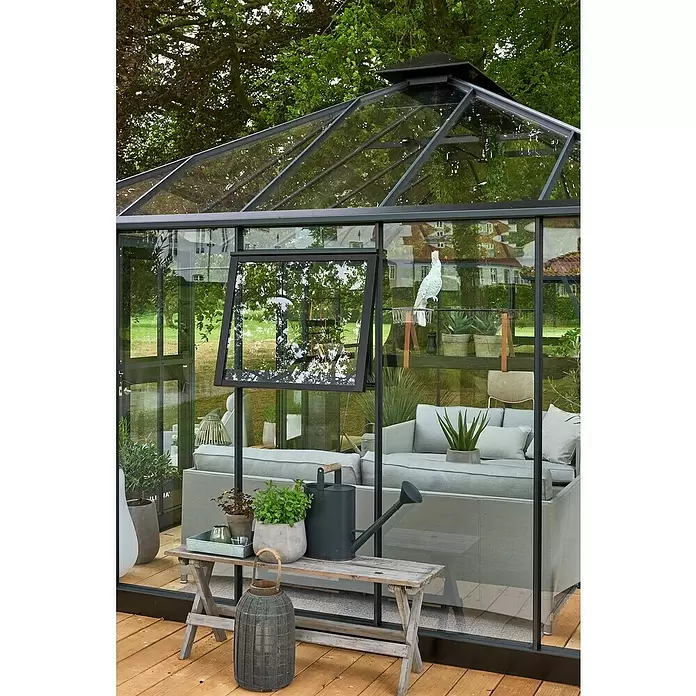 Juliana Gewächshaus Grand Oase - Außenmaß inkl. Dachüberstand (B x T): 511 x 368 cm, Material Seitenwand: Glas, 3 mm, Anthrazit - Gewächshaus aus dunklem Metall und Glas, als elegantes Wohnzimmer im Freien mit Sofas und Pflanzen auf Holzterrasse.