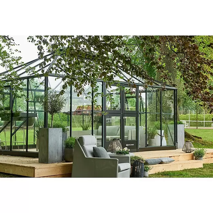 Juliana Gewächshaus Grand Oase - Außenmaß inkl. Dachüberstand (B x T): 511 x 368 cm, Material Seitenwand: Glas, 3 mm, Anthrazit - Modernes Gewächshaus aus Glas mit dunklem Rahmen auf Holzterrasse, als eleganter Outdoor-Wohnbereich mit Möbeln.