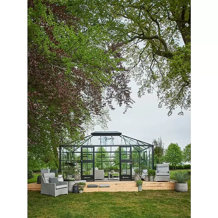 Juliana Gewächshaus Grand Oase - Außenmaß inkl. Dachüberstand (B x T): 511 x 368 cm, Material Seitenwand: Glas, 3 mm, Anthrazit - Ein großes, modernes Gewächshaus aus Glas mit schwarzem Rahmen und Sitzgelegenheiten innen und außen auf einer Holzterrasse im Garten.
