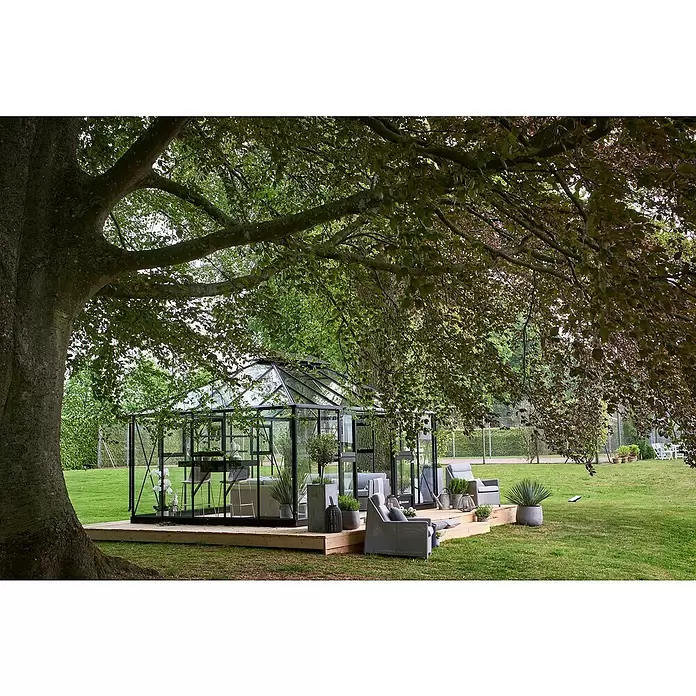 Juliana Gewächshaus Grand Oase - Außenmaß inkl. Dachüberstand (B x T): 511 x 368 cm, Material Seitenwand: Glas, 3 mm, Anthrazit - Schwarzgerahmtes Glasgewächshaus auf Holzterrasse im Garten, als Wohnbereich eingerichtet.