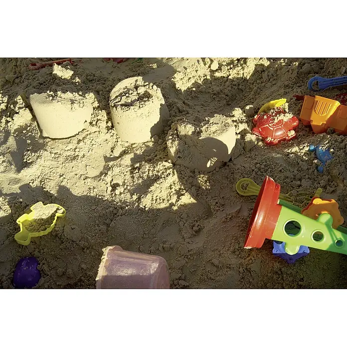 Kinderspielsand - 25 kg - Nahaufnahme von Sandburgen und bunten Förmchen in einem Sandkasten, die zu kreativem Spiel anregen.