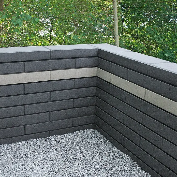 Christoph Mauerstein C-Line - Grau, 50 x 25 x 10 cm, Beton - Eine stilvolle Mauer aus anthrazitfarbenen Pflastersteinen mit einer grauen Akzentreihe und einer Kiesfläche im Garten. Perfekt für moderne Gartendesigns.