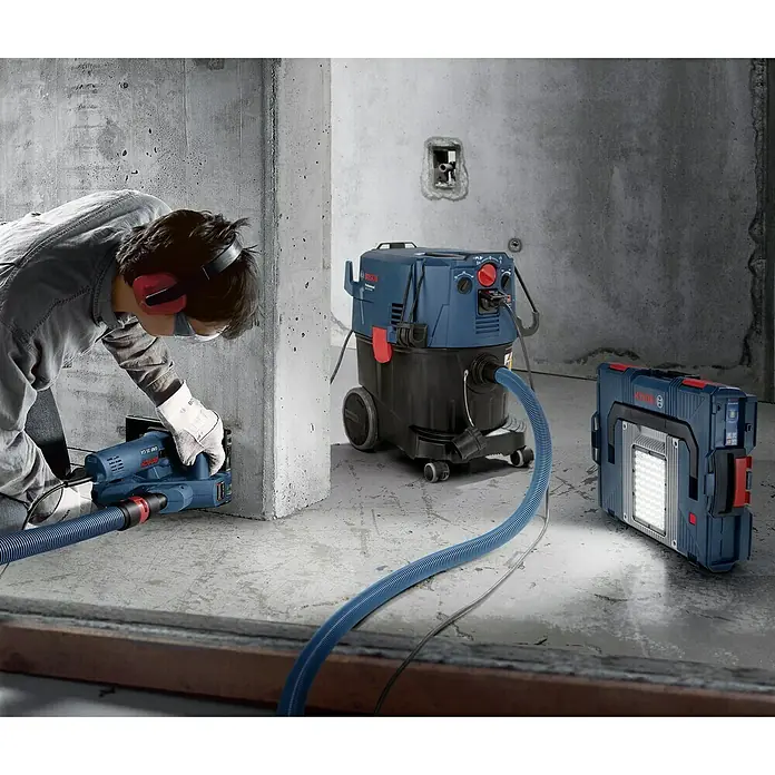 Bosch Professional Elektro-Nass- & Trockensauger GAS 35 M AFC - 1.200 W, Behältervolumen: 35 l, Mit Beutel - Ein Bauarbeiter benutzt einen Bosch Mauernutfräse mit Staubsauger, während eine Bosch Arbeitsleuchte für Helligkeit sorgt.