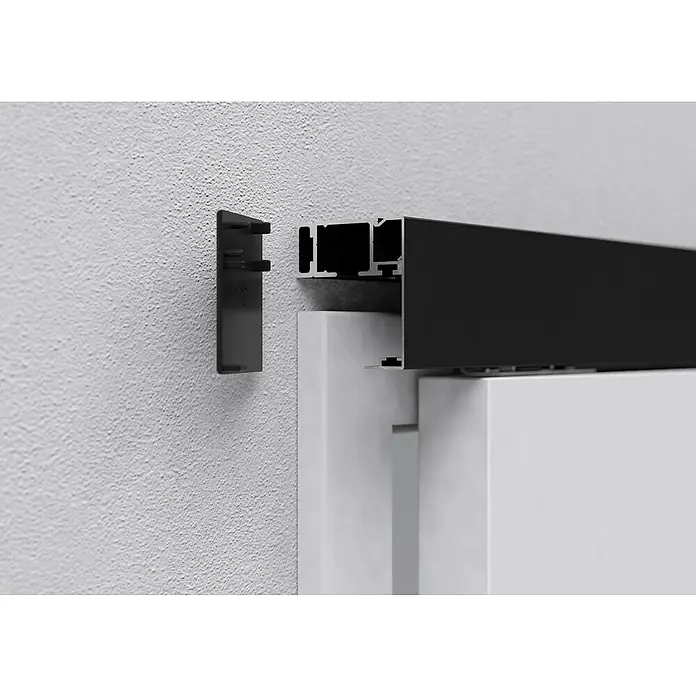 Entravia Abstands-Set Bright-Slide - Schwarz eloxiert, 2.000 mm, Passend für: Entravia Bright-Slide Schiebetüren vor der Wand laufend - Nahaufnahme einer schwarzen Wandhalterung für Schiebetüren, die neben einer weißen Tür an einer strukturierten Wand befestigt ist.