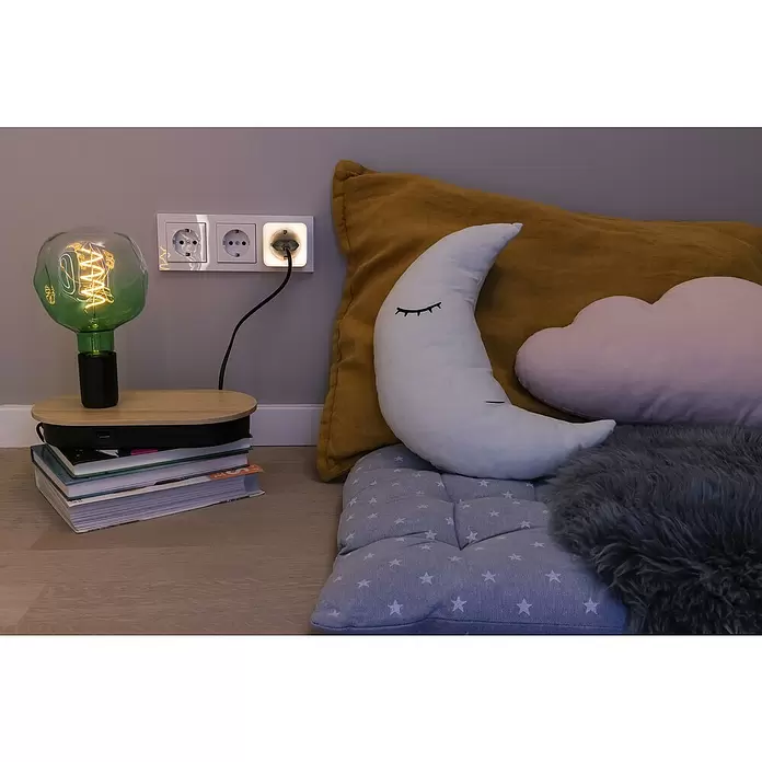 Ledvance Smart+ WiFi LED-Nachtlicht - L x B x H: 57 x 84 x 57 mm - Grüne Glastischlampe auf Holztisch, beleuchtet eine gemütliche Lese-Ecke am Boden mit Mond- und Wolkenkissen und einem Fellteppich.