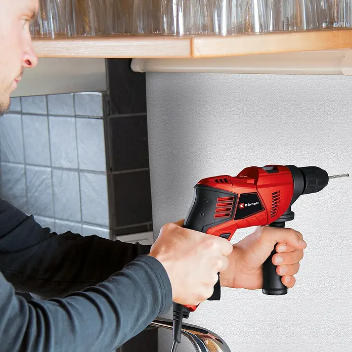 Einhell Classic Schlagbohrmaschine TE-ID 500 E - 550 W, Schnellspannbohrfutter - Nahaufnahme eines Mannes, der eine rote Einhell Schlagbohrmaschine verwendet, um in eine Wand zu bohren.