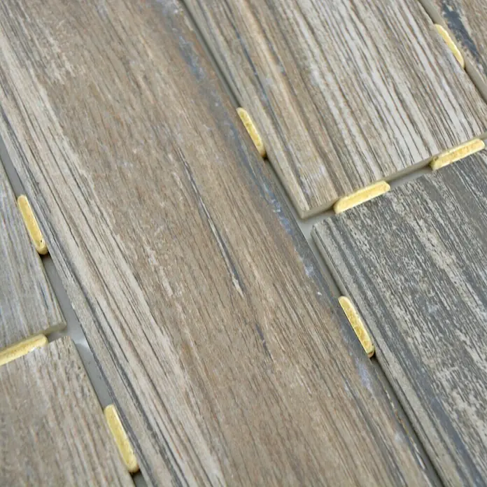 Mosaikfliese Brick Oak Mink CDJ 09BR - 25,2 x 36,7 cm, Dunkelbraun, Matt - Nahaufnahme von Holzmaserungfliesen, die mit gelben Abstandshaltern verlegt werden. Die Textur der Fliesen ist deutlich sichtbar.