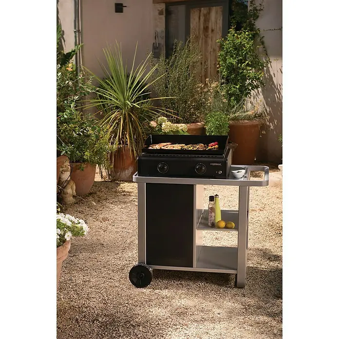 Campingaz Barbacoa de gas Othello - Superficie de la parrilla (An x Pr): 58 x 36 cm, 6 kW, Número de quemadores: 2 - Una parrilla de gas negra de Campingaz lista para cocinar en un patio, con botones y estantes para fácil almacenamiento.
