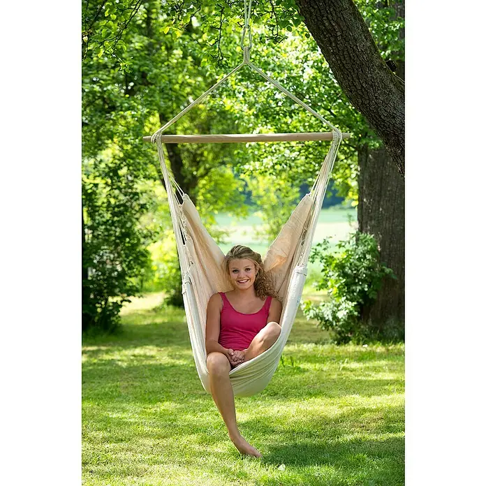 Amazonas Stabhängematte Brasil Natura - L x B: 160 x 130 cm, Textil, Beige - Eine junge Frau entspannt in einer Hängeinsel aus Baumwolle im Garten, die an einem Baum befestigt ist. Ideal für gemütliche Stunden im Freien.