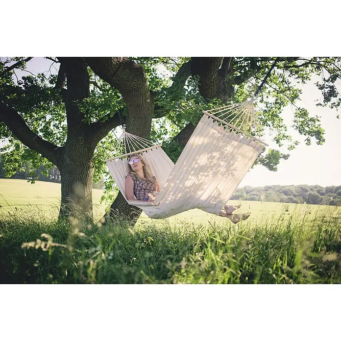 Amazonas Doppelstabhängematte Tobago - L x B: 270 x 150 cm, Textil, Beige - Frau entspannt in einer Hängematte zwischen Bäumen, umgeben von grüner Natur. Die Hängematte bietet Komfort und Entspannung im Freien.