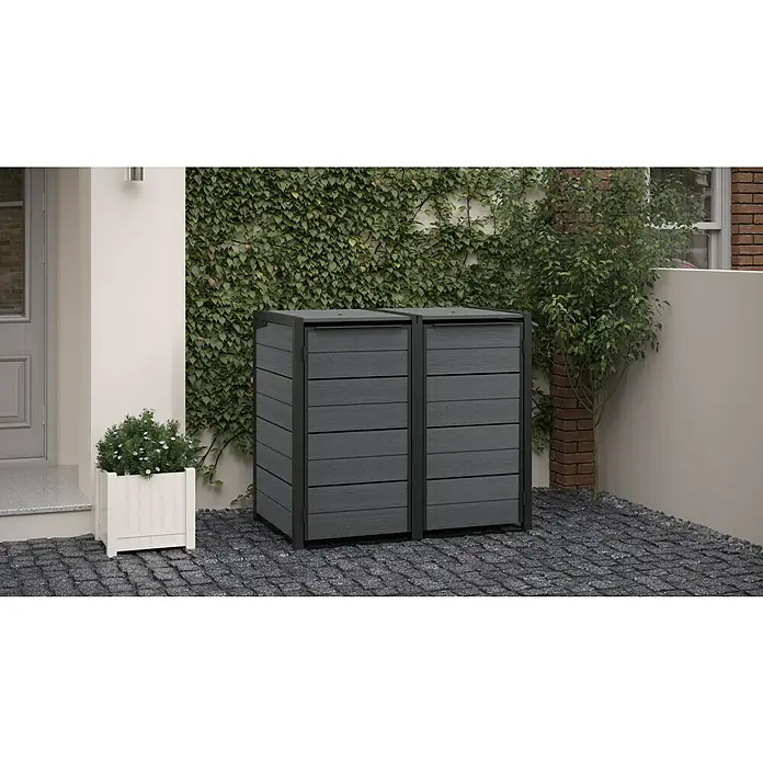 Keter Mülltonnenbox Hide Away - Kunststoff, Grau - Eine Doppel-Mülltonnenbox aus grauem Holzimitat steht auf einem gepflasterten Hof, ideal für stilvolle Müllentsorgung im Freien.