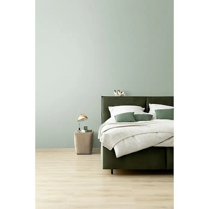 SCHÖNER WOHNEN-Farbe Wandfarbe Designfarbe - Harmonisches Jadegrün, Matt, 1 l, Konservierungsmittelfrei - Schlafzimmer mit einem eleganten grünen Bett, einem Beistelltisch mit Lampe und einer hellgrünen Wand. Die Einrichtung strahlt Ruhe und Komfort aus.