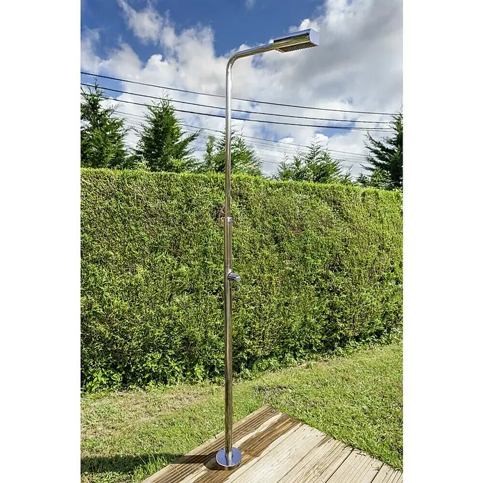 Gre Ducha de jardín Minimal - Altura: 216 cm, Acero inoxidable, Plateado - Una elegante ducha de exterior de acero inoxidable con cabezal rectangular se alza sobre una plataforma de madera frente a un seto verde.