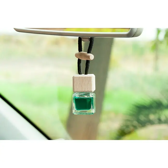 Ambientador de coche para colgar - Mentolado, 8 sem. - Primer plano de un ambientador de coche con aceite de fragancia verde que cuelga de un espejo retrovisor para una experiencia de conducción agradable.