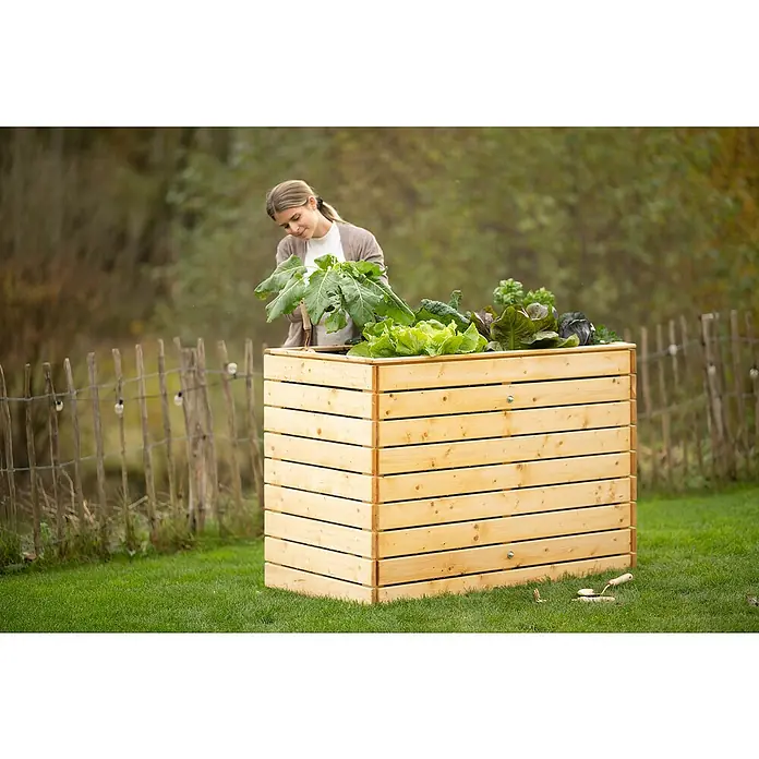 Westmann Hochbeet Asket L - 70 x 130 x 90 cm, Holz, Natur - Ein Hochbeet aus Holz, bepflanzt mit verschiedenen Gemüsesorten, steht auf einem grünen Rasen. Eine junge Frau kümmert sich um die Pflanzen.