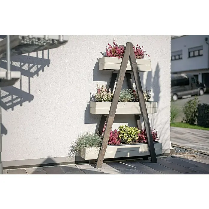 Westmann Hochbeet Ella - L x B x H: 101 x 25 x 147 cm, Holz, Grau/Weiß - Eine dreistufige Pflanzenleiter aus Holz mit bunten Blumen in weißen Pflanzkästen, die an einer weißen Wand steht und eine Gartenecke schmückt.
