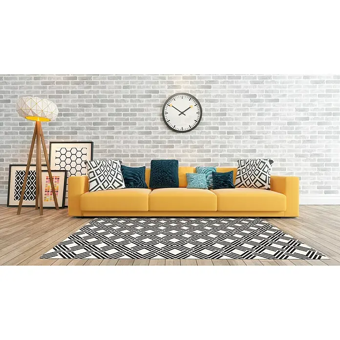 Alfombra de vinilo Living geométrica - Negro, 200 x 140 cm - Sofá amarillo con cojines decorativos frente a una pared de ladrillo blanco y una alfombra geométrica.