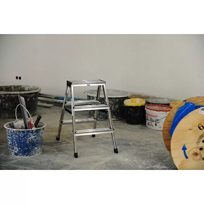 Krause Monto Escalera de tijera de doble acceso - Altura de trabajo: 2,2 m, Número de peldaños: 6 ud., Carga soportada: 150 kg, Aluminio - Escalera plegable de aluminio plateado con tres peldaños, en una habitación en renovación con herramientas de construcción.